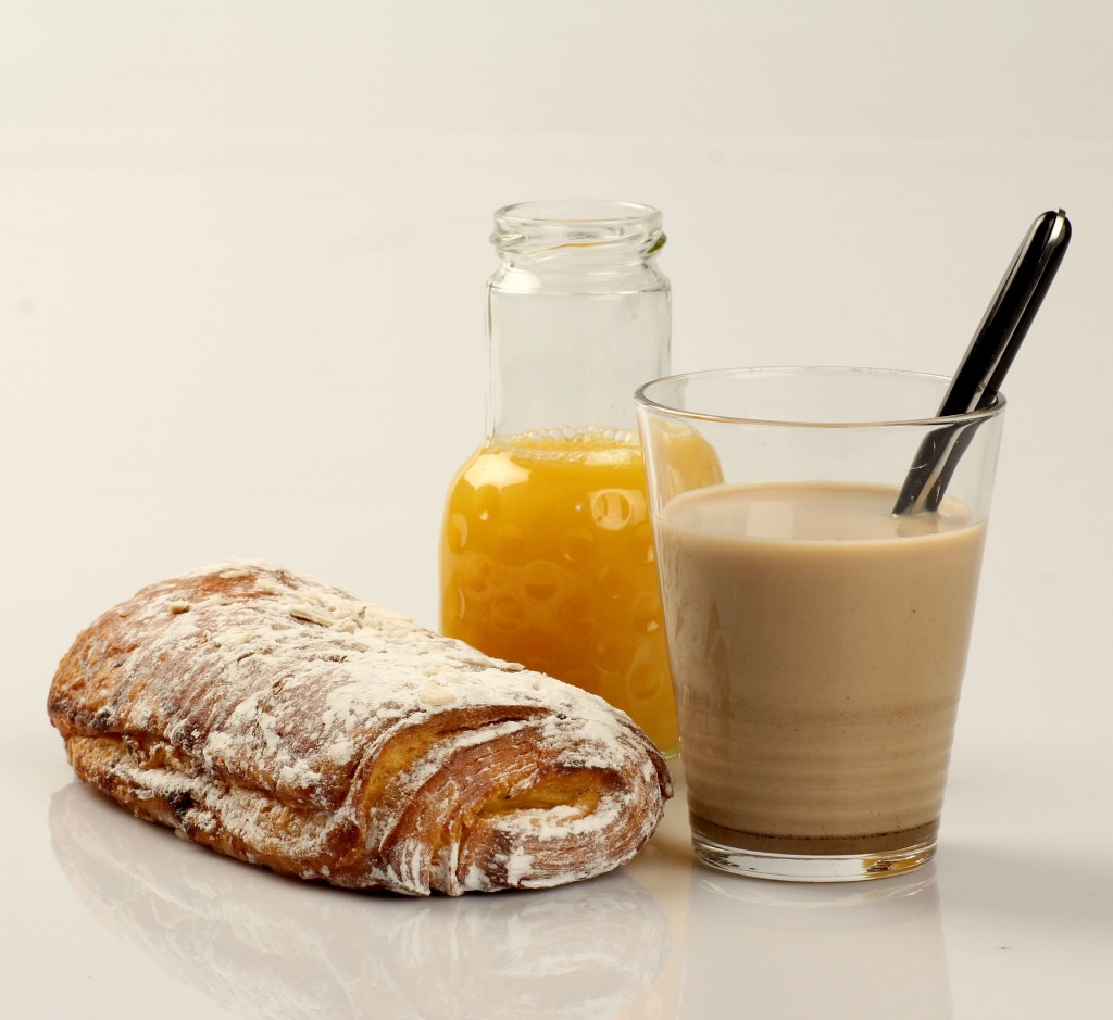 Desayuno formado por un zumo de naranja, un vaso de leche con cacao en polvo y una napolitana