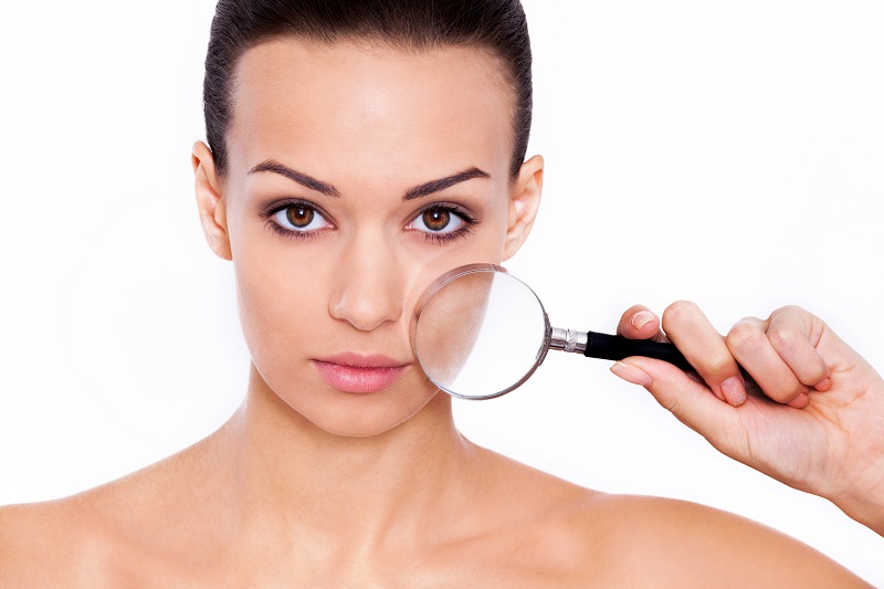 Magnifying facial features. Studio shot of a beautiful woman with a magnifying glass in front of her face